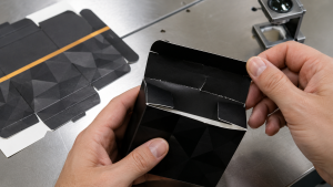 Pemeriksaan karton cetak yang menunjukkan retak pada area lipatan setelah proses die cut dan folding.